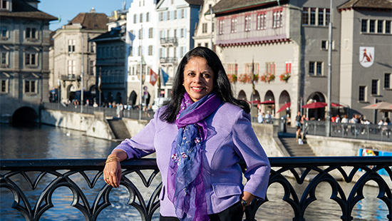 Barbara Rubel in light purple sweater and dark purple scarf poses on a bridge in Switzerland