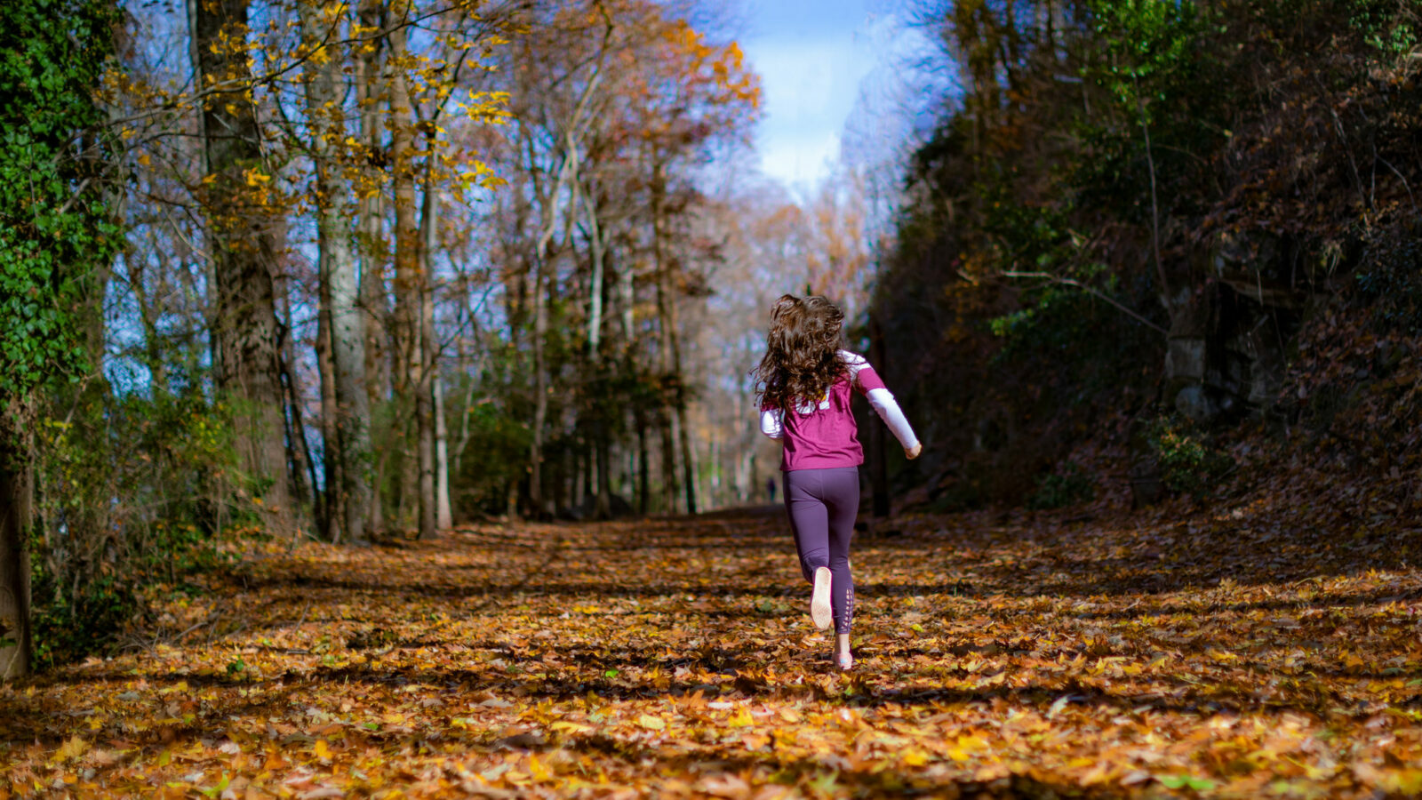 A person runs down the Vulcan Trail. Autumn leaves cover the ground.