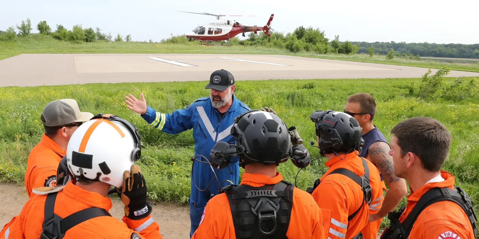 A group of men in orange listen to a pilot in blue