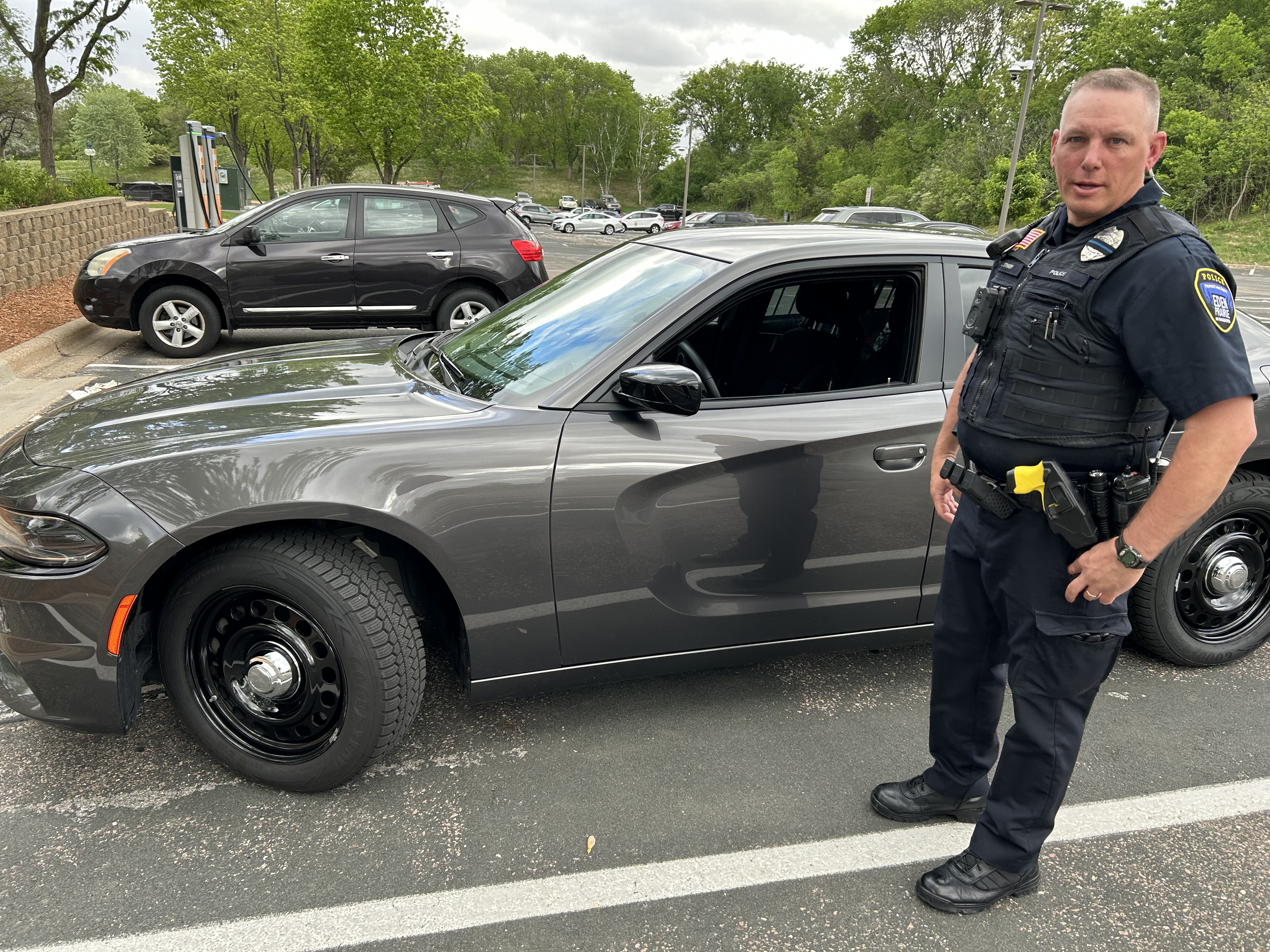 Officer stands next to grey squad vehicle.