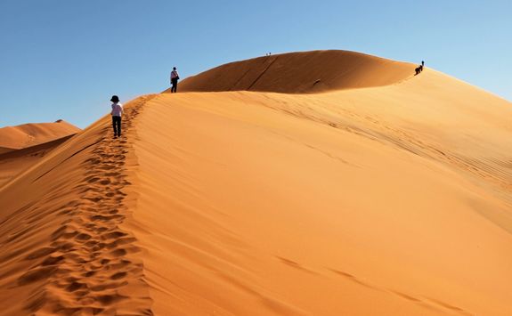 people climbing red sand dunes