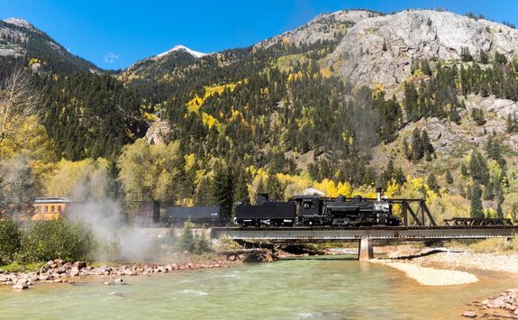 Steam locomotive crossing river and mountain background