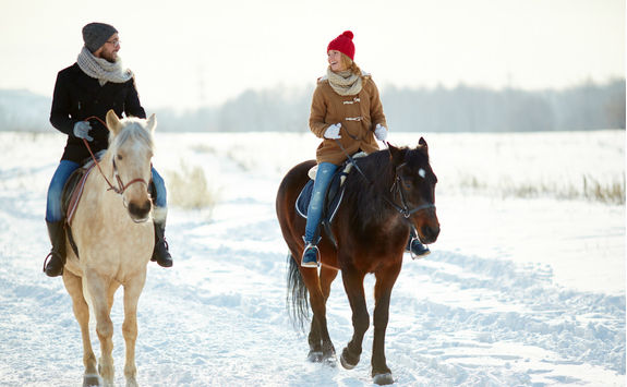 couple horseback riding along snowy trail