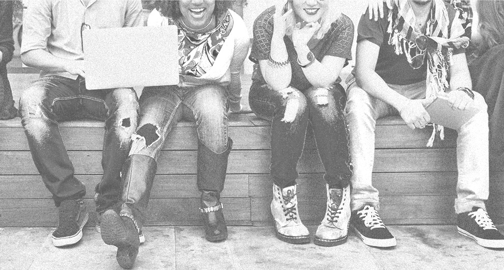 Five people sitting on a bench smiling while one holds a laptop.
