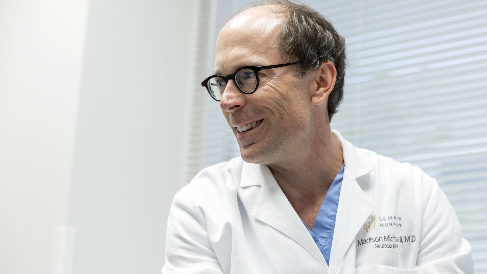 A doctor in a lab coat and glasses smiling and looking to the left