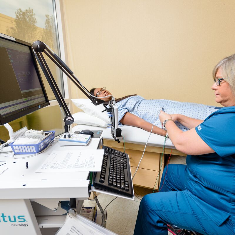 Nurse conducting an EMG on a patient's arm while the patient lays on their back