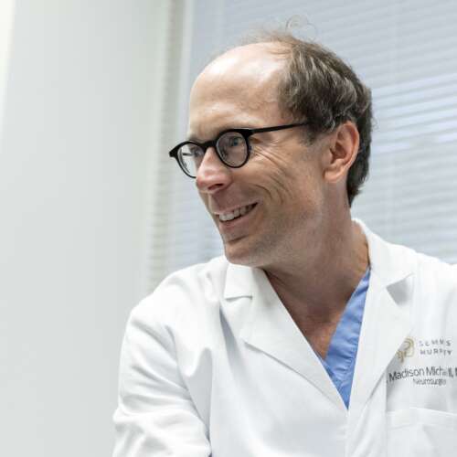 A doctor in a lab coat and glasses smiling and looking to the left
