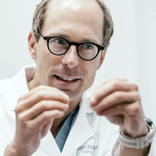 A doctor's face in glasses with his hands up to describe something