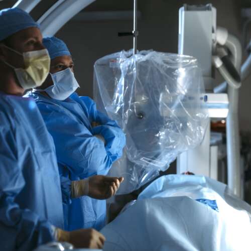 Two doctors standing in a surgery room looking at image guided surgery with patient in foreground