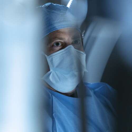 Blue image with a doctor's face in scrubs and mask slightly blurred