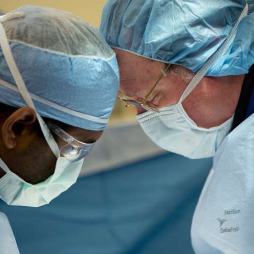 Two doctors with masks and scrubs with their heads touching looking down in surgery