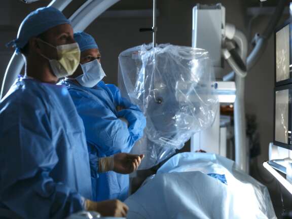 Two doctors standing in a surgery room looking at image guided surgery with patient in foreground