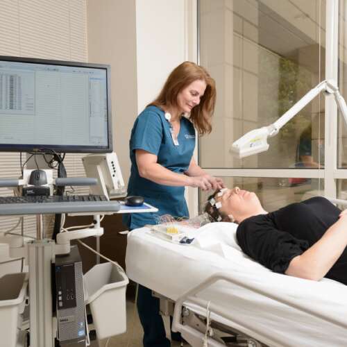 Nurse placing wires on a patient's head with a computer in the forwground