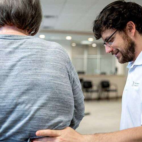 Back of a woman with a physical therapist guiding her back with his hand
