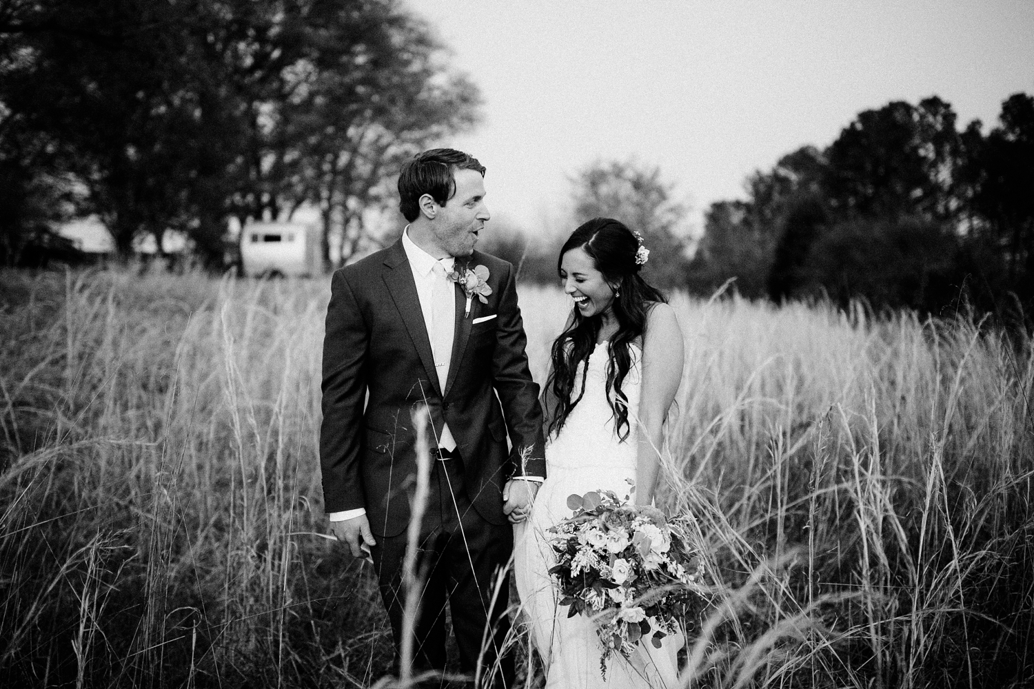 bride and groom in field holding hands