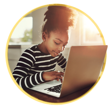 A young girl with her hair in a bun, wearing a striped shirt, intently uses a laptop at a desk in a warmly lit room, participating in an agriculture entrepreneurship program.