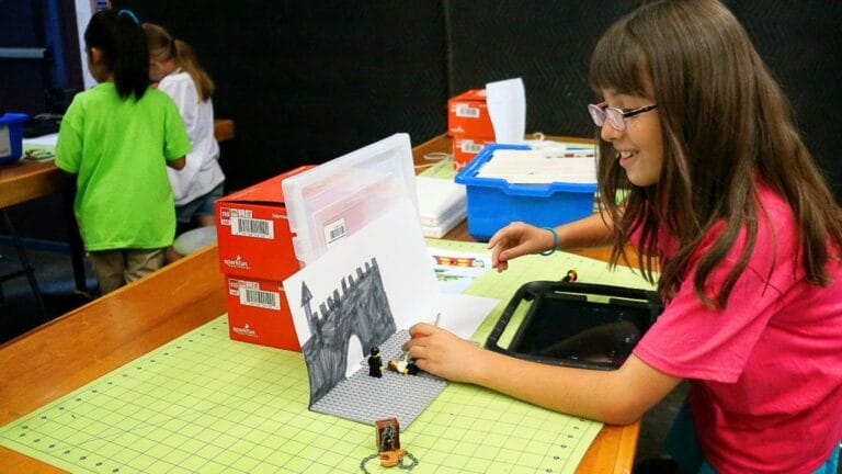 Young girl using lego bricks and hand-drawn backdrop to create a stop-motion video