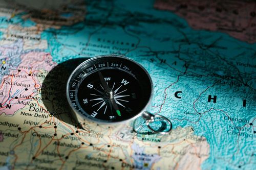 Close-up of a black compass placed on a world map, symbolizing financial direction and planning for irregular income with a calendar budget app.