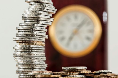 Stack of coins in front of a blurred clock symbolizing time and money management, representing budgeting, saving, and cash flow planning.