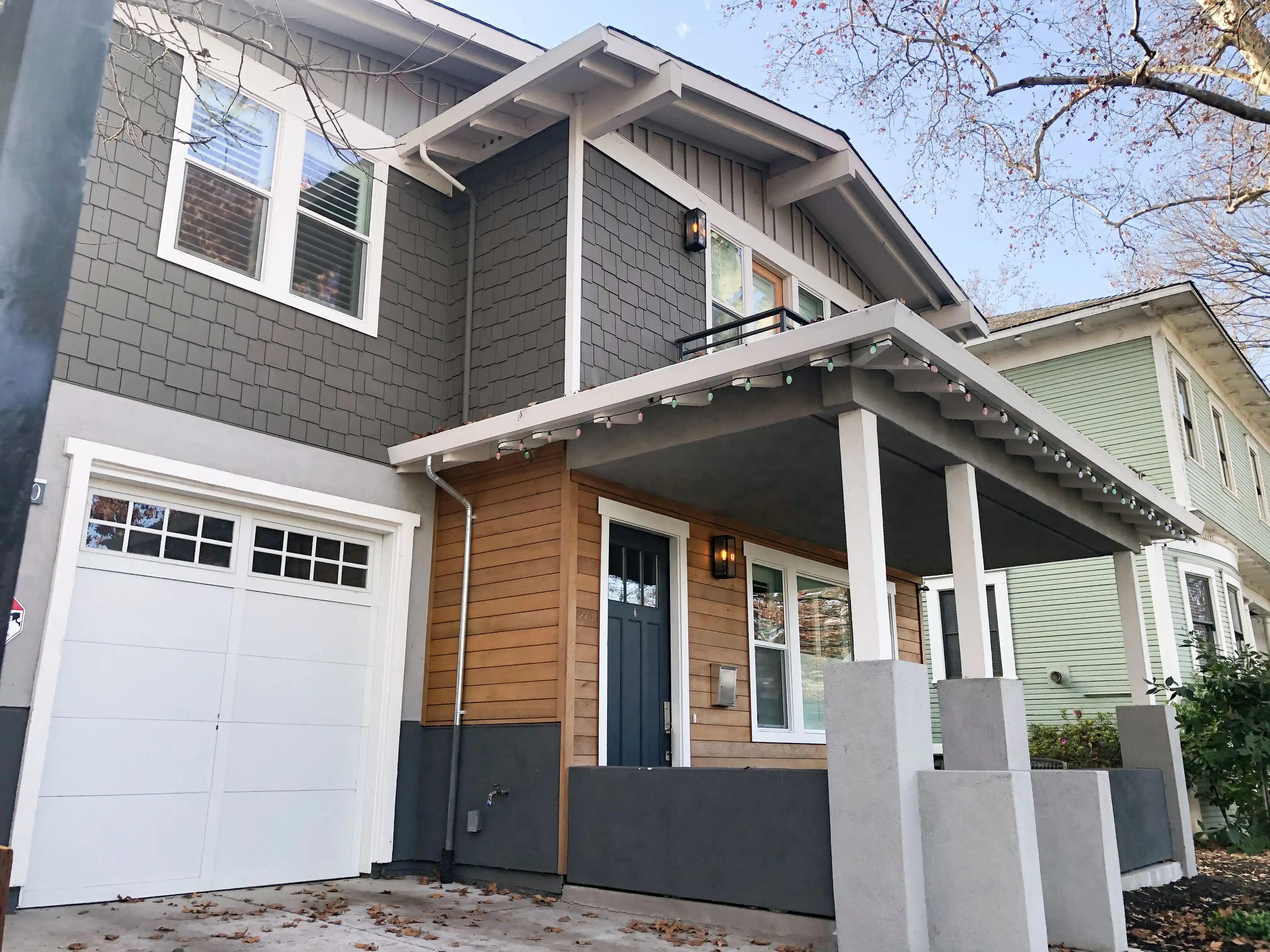 A modern house facade with a combination of gray and brown siding, white garage door, and small porch with columns. A modern house facade with a combination of gray and brown siding, white garage door, and small porch with columns.