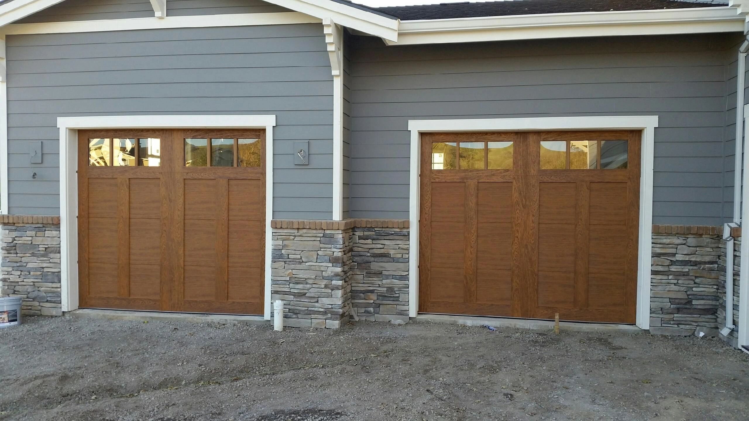 Two wood-paneled garage doors installed on a gray home with stone accents Two wood-paneled garage doors installed on a gray home with stone accents