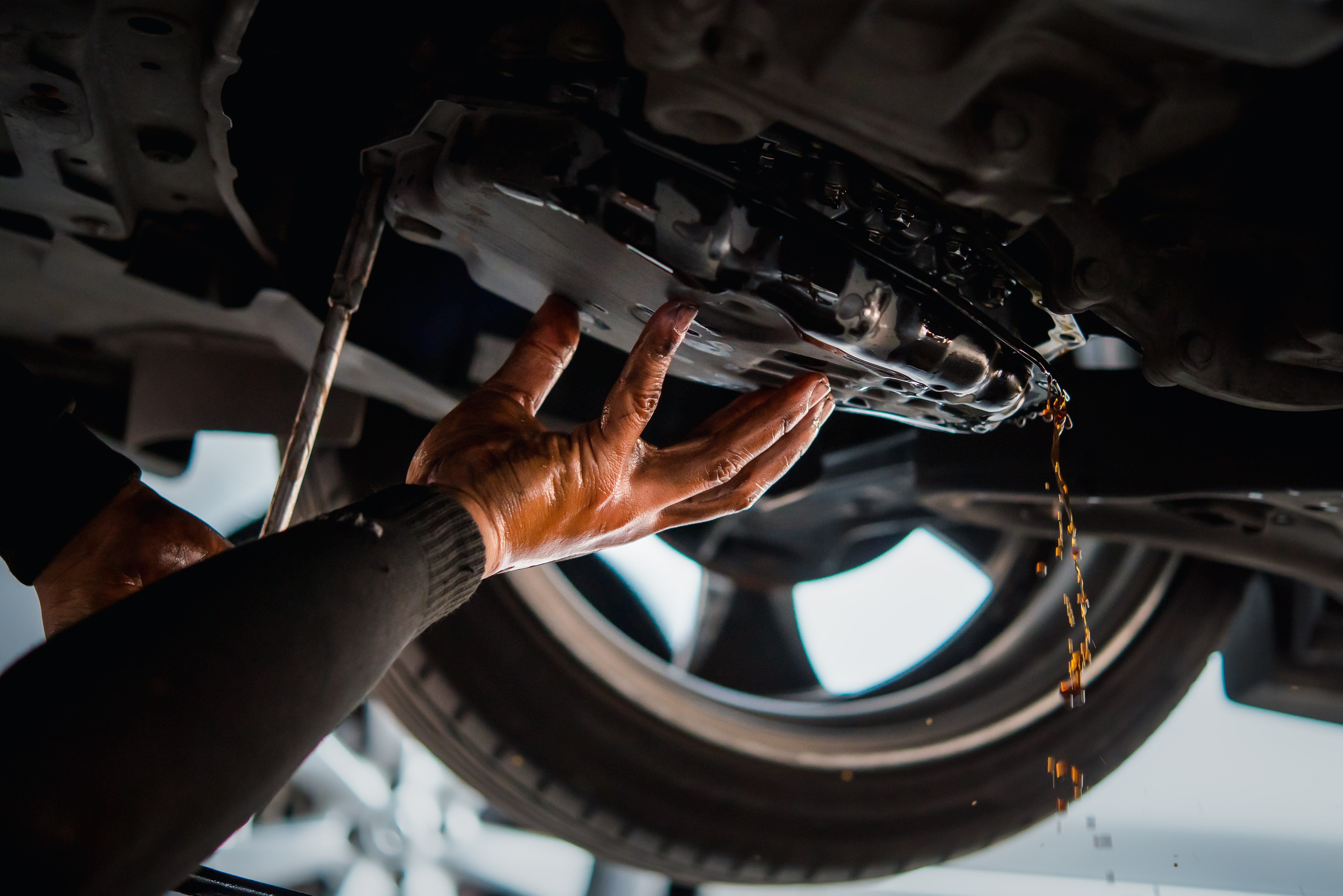  Close-up of mechanic's hands working on a car's undercarriage with fluid dripping, showcasing precision and attention to detail.