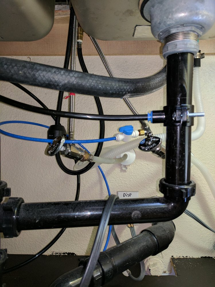 Close-up of a plumbing system under a sink, featuring various pipes, hoses, and connectors against a wall backdrop. Close-up of a plumbing system under a sink, featuring various pipes, hoses, and connectors against a wall backdrop.