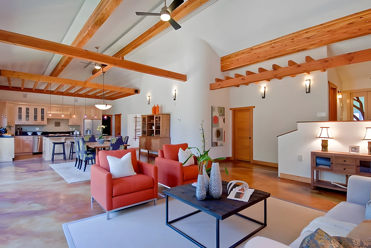 A spacious living area with exposed wood beams, orange armchairs, a wooden coffee table, and a view of the kitchen area. Decor is modern with a focus on natural materials. A spacious living area with exposed wood beams, orange armchairs, a wooden coffee table, and a view of the kitchen area. Decor is modern with a focus on natural materials.