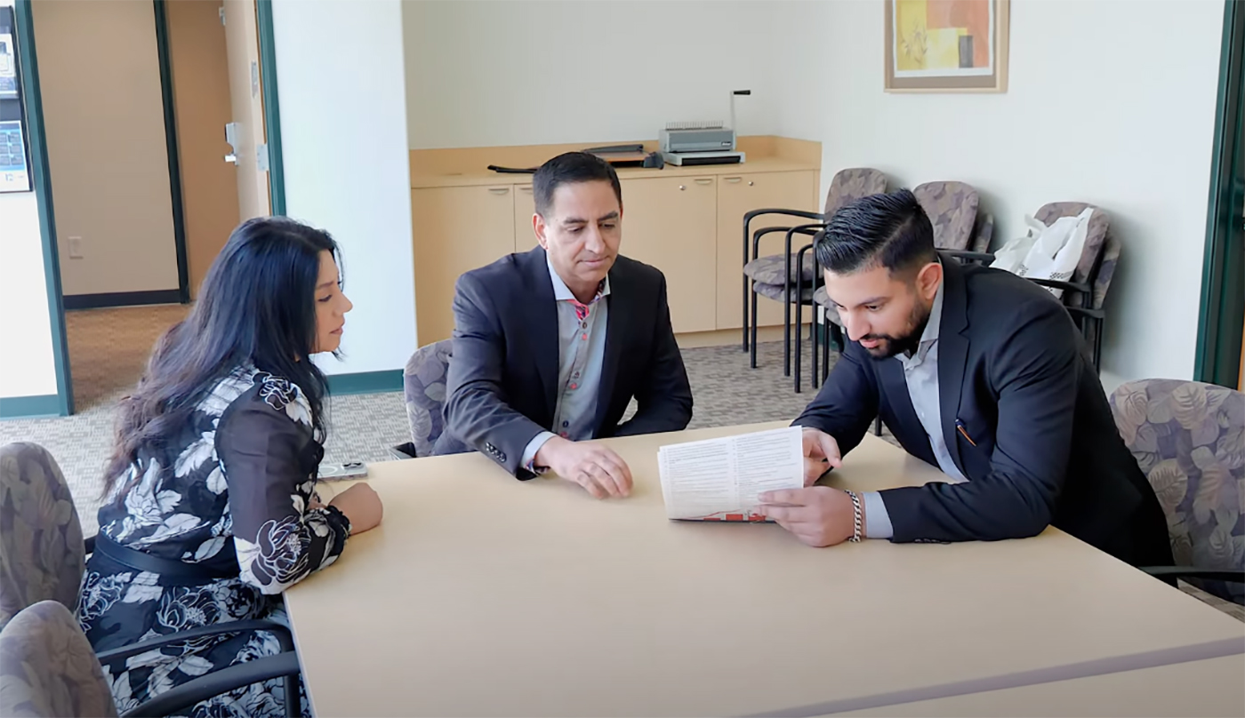  Three people in a conference room sit at a table reviewing a document together, surrounded by office chairs and furnishings.