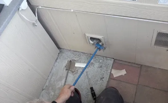 A person uses a blue brush to clean a wall vent. Nearby are various tools on a concrete and tile surface. A person uses a blue brush to clean a wall vent. Nearby are various tools on a concrete and tile surface.