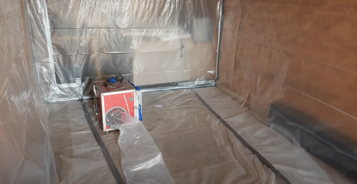 A red dehumidifier or air filtration device is placed inside a plastic-sheeted containment area for environmental safety work. A red dehumidifier or air filtration device is placed inside a plastic-sheeted containment area for environmental safety work.