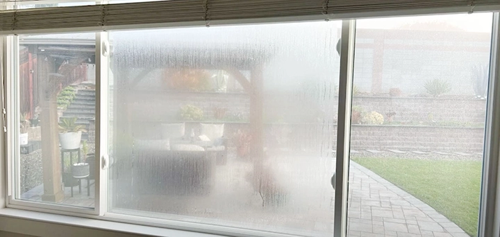Fogged window partially obscuring a view of an outdoor patio with chairs and plants, framed by a pergola. Fogged window partially obscuring a view of an outdoor patio with chairs and plants, framed by a pergola.