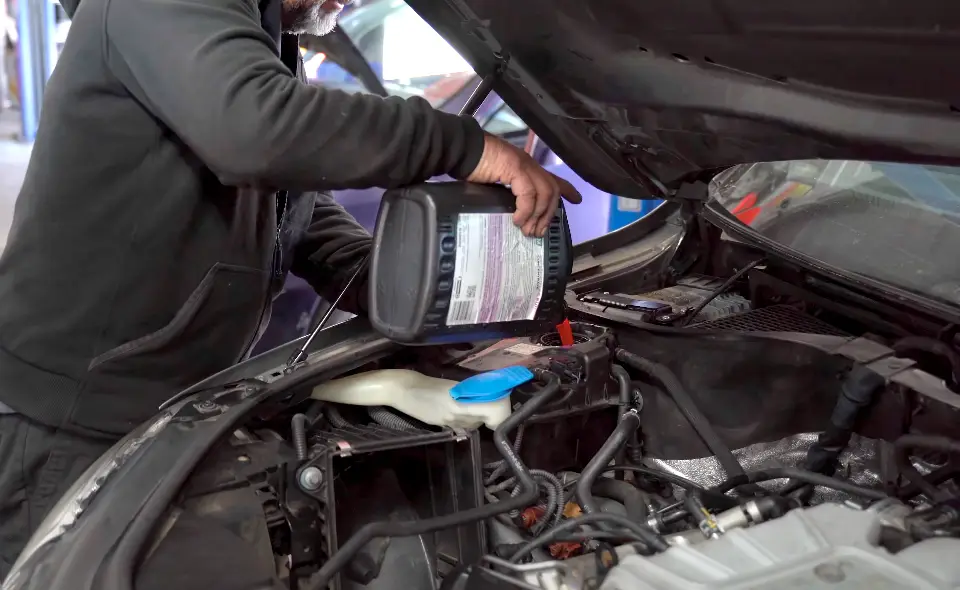 A technician pours engine oil into a car engine with the hood open, focusing on careful work. A technician pours engine oil into a car engine with the hood open, focusing on careful work.