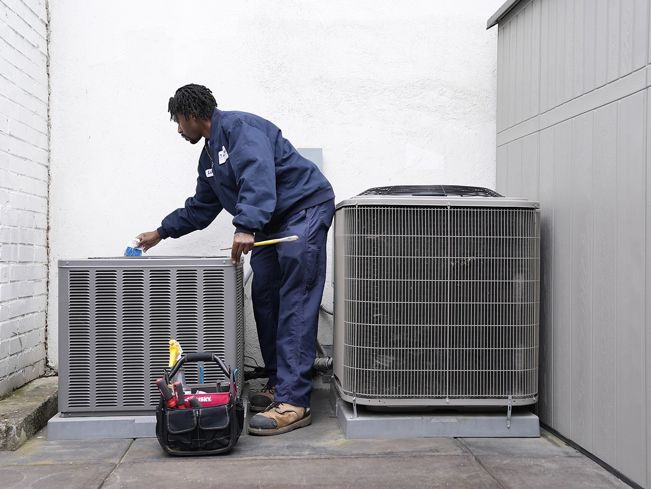 In this image, a skilled HVAC technician is carefully installing a new air conditioning unit. The technician is shown wearing a blue uniform and gloves, ensuring safety and precision during the installation process. The unit is mounted on a wall bracket outside a building, ready to provide efficient cooling. This setup exemplifies Hassler Heating & Air Conditioning LLC’s commitment to quality workmanship and reliable climate control solutions for residential or commercial properties. In this image, a skilled HVAC technician is carefully installing a new air conditioning unit. The technician is shown wearing a blue uniform and gloves, ensuring safety and precision during the installation process. The unit is mounted on a wall bracket outside a building, ready to provide efficient cooling. This setup exemplifies Hassler Heating & Air Conditioning LLC’s commitment to quality workmanship and reliable climate control solutions for residential or commercial properties.