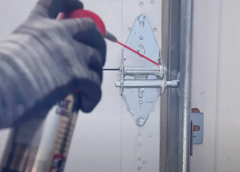 Gloved hand applying lubricant to a garage door hinge with a spray can. Gloved hand applying lubricant to a garage door hinge with a spray can.