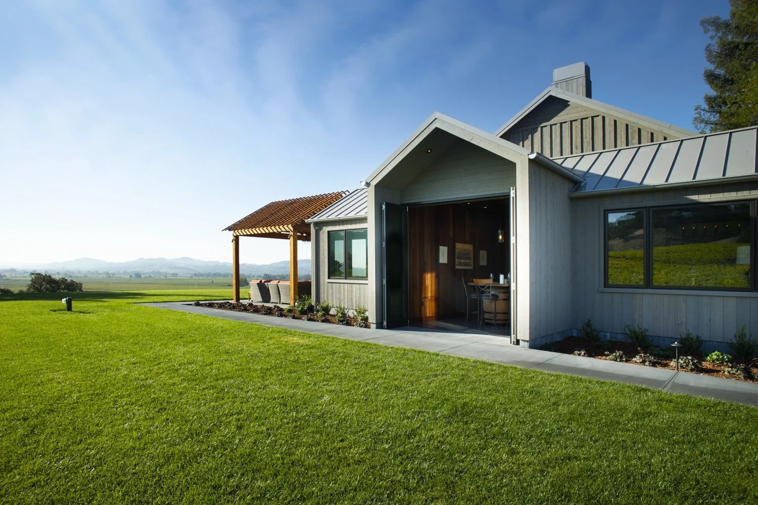 Modern ranch house with open patio and lush lawn, set against a backdrop of expansive fields and distant mountains.
``` Modern ranch house with open patio and lush lawn, set against a backdrop of expansive fields and distant mountains.
```
