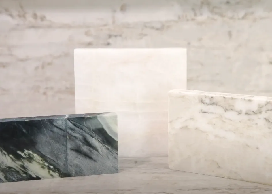 Close-up of three marble slabs with distinct veining patterns on a textured stone background. Close-up of three marble slabs with distinct veining patterns on a textured stone background.
