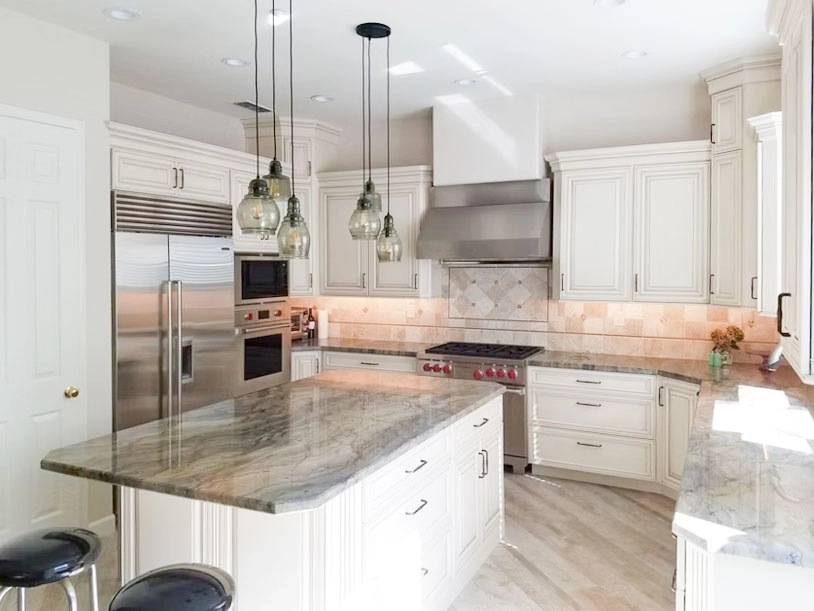 Modern kitchen with marble countertops, pendant lights, stainless steel appliances, and white cabinetry. Modern kitchen with marble countertops, pendant lights, stainless steel appliances, and white cabinetry.