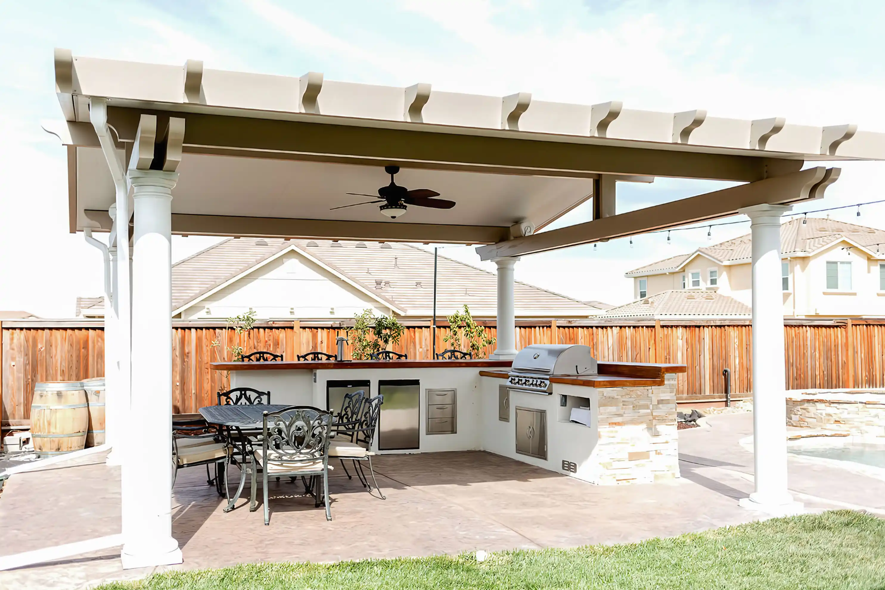 Outdoor patio with a covered seating area, grill, and dining set under a structured patio cover, with homes and fence in the background. Outdoor patio with a covered seating area, grill, and dining set under a structured patio cover, with homes and fence in the background.