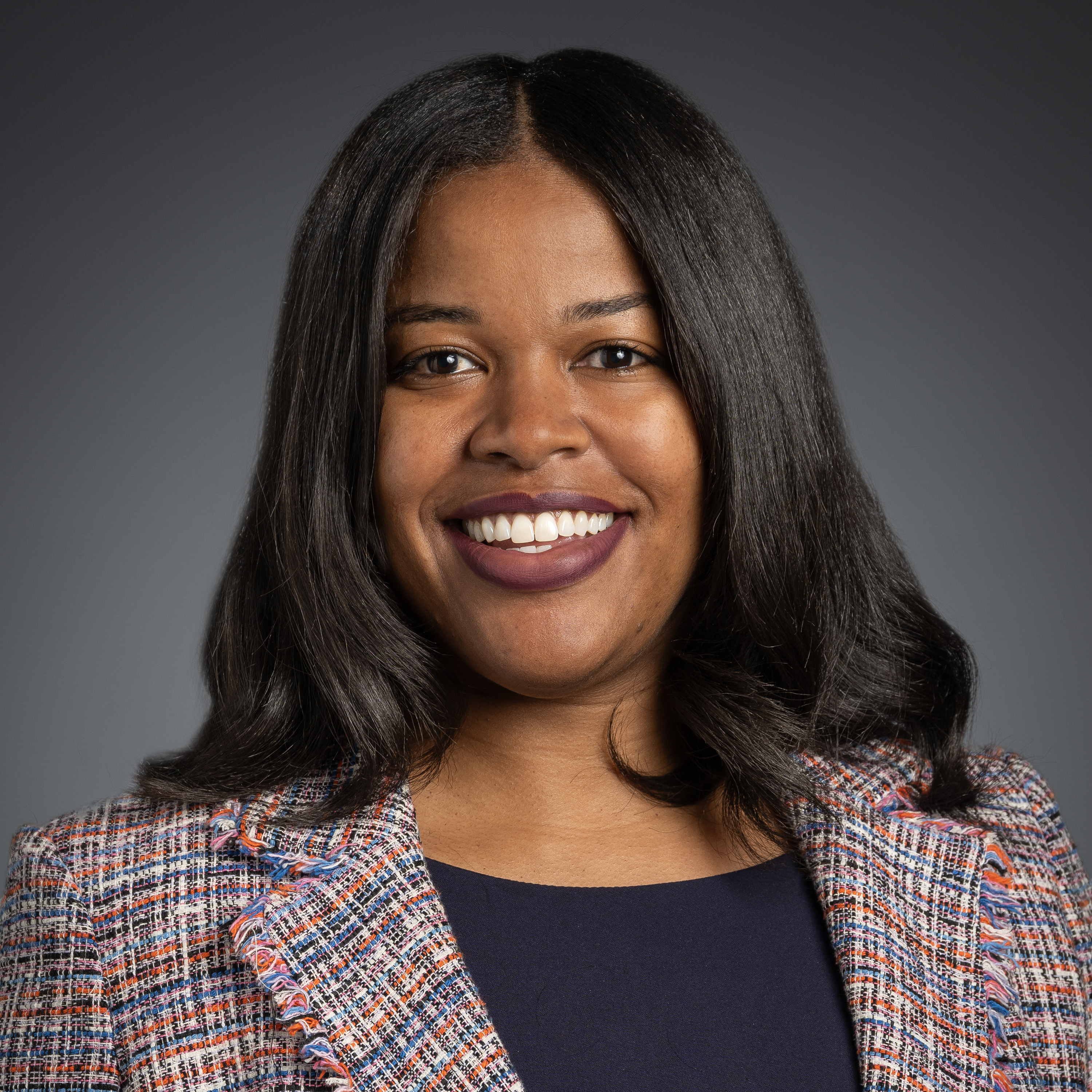 Headshot of Ciare James wearing a patterned blazer against a gray background.