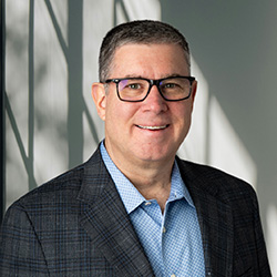 Headshot of James J. Kavanaugh wearing a light blue button up shirt and dark gray  suit jacket
