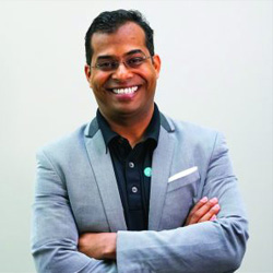 Headshot of Venkatesh Ganapathy wearing a black button up  shirt and light blue suit jacket