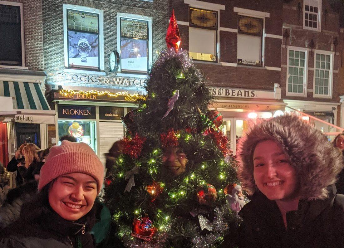 Two students pose outside with a decorated Christmas tree