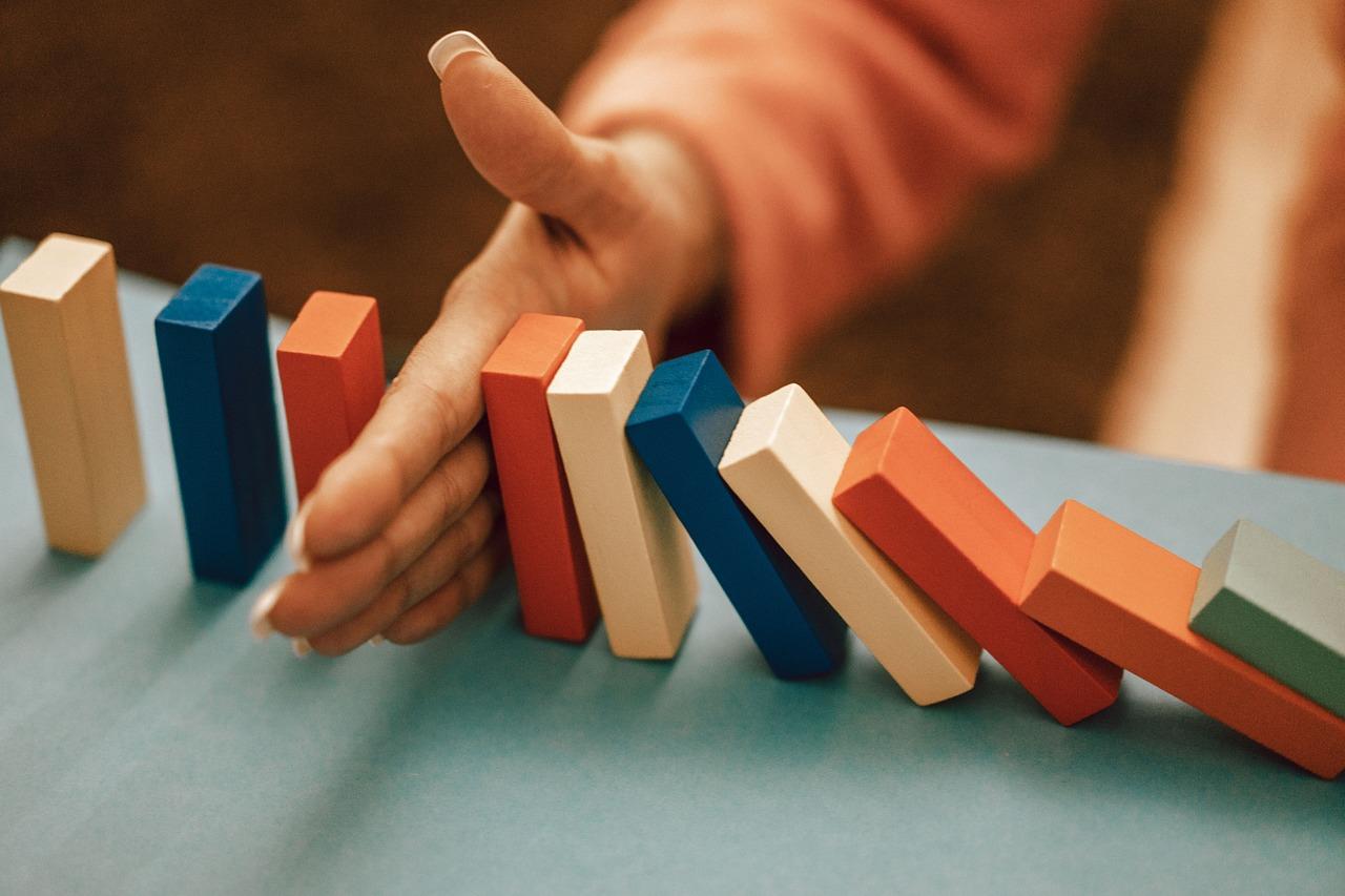 A hand is positioned to stop a row of wooden dominoes from falling
