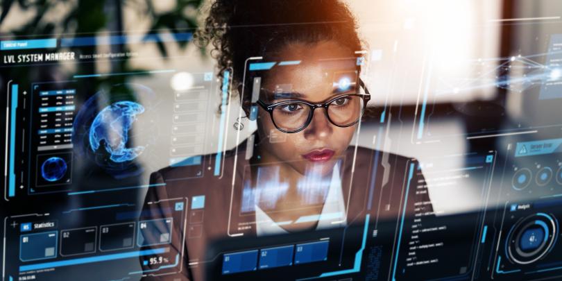 Person at a transparent screen with blue digital interfaces showing globe, charts and system data.