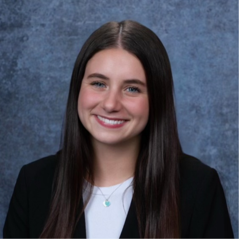 Bree smiling wearing a suit in front of a blue background