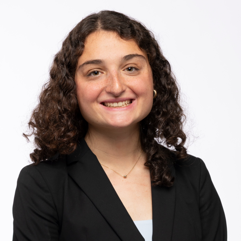 Sarah smiling wearing a suit with a simple white background