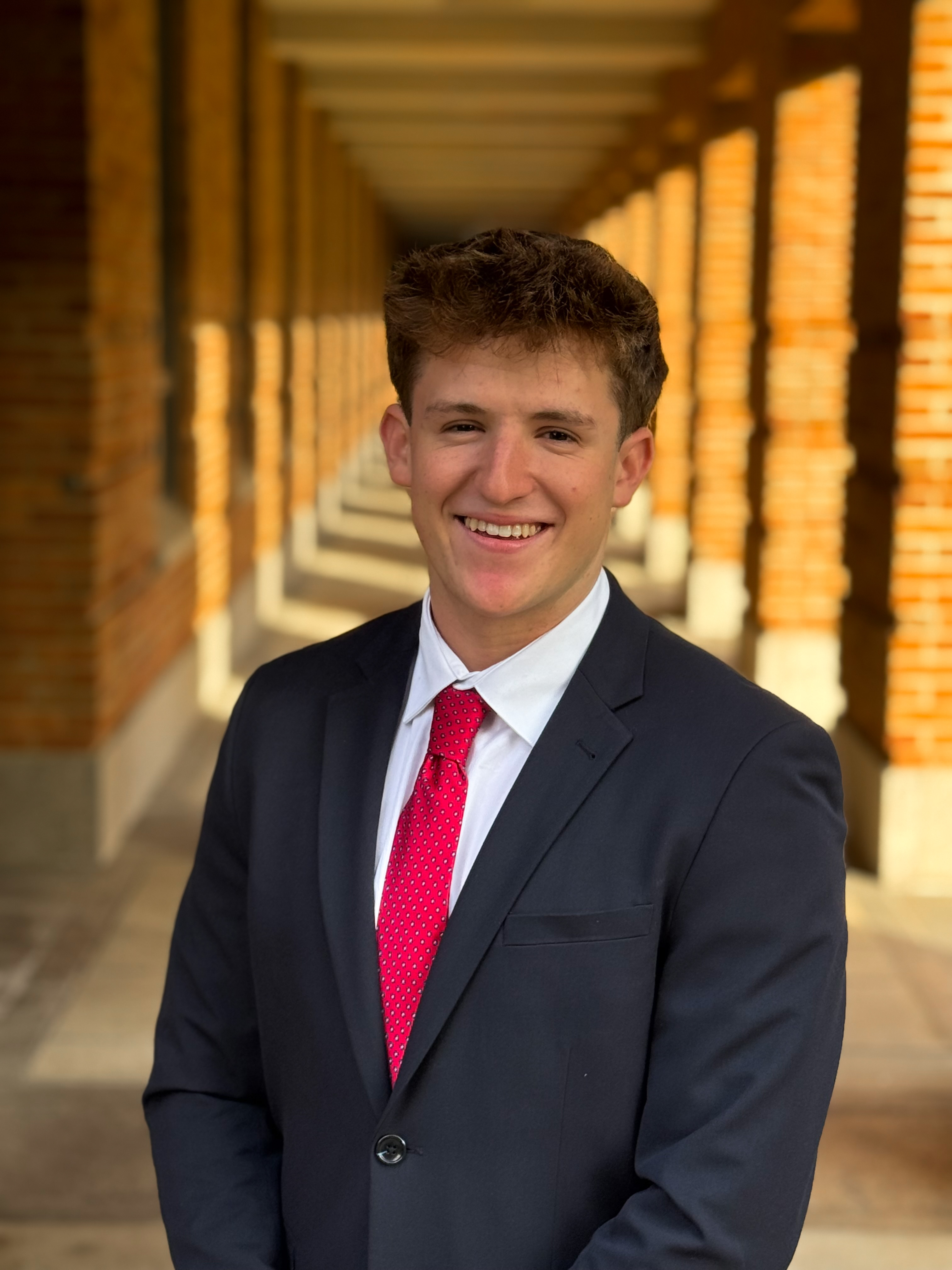 man smiling at the camera with dark blue suit and red tie
