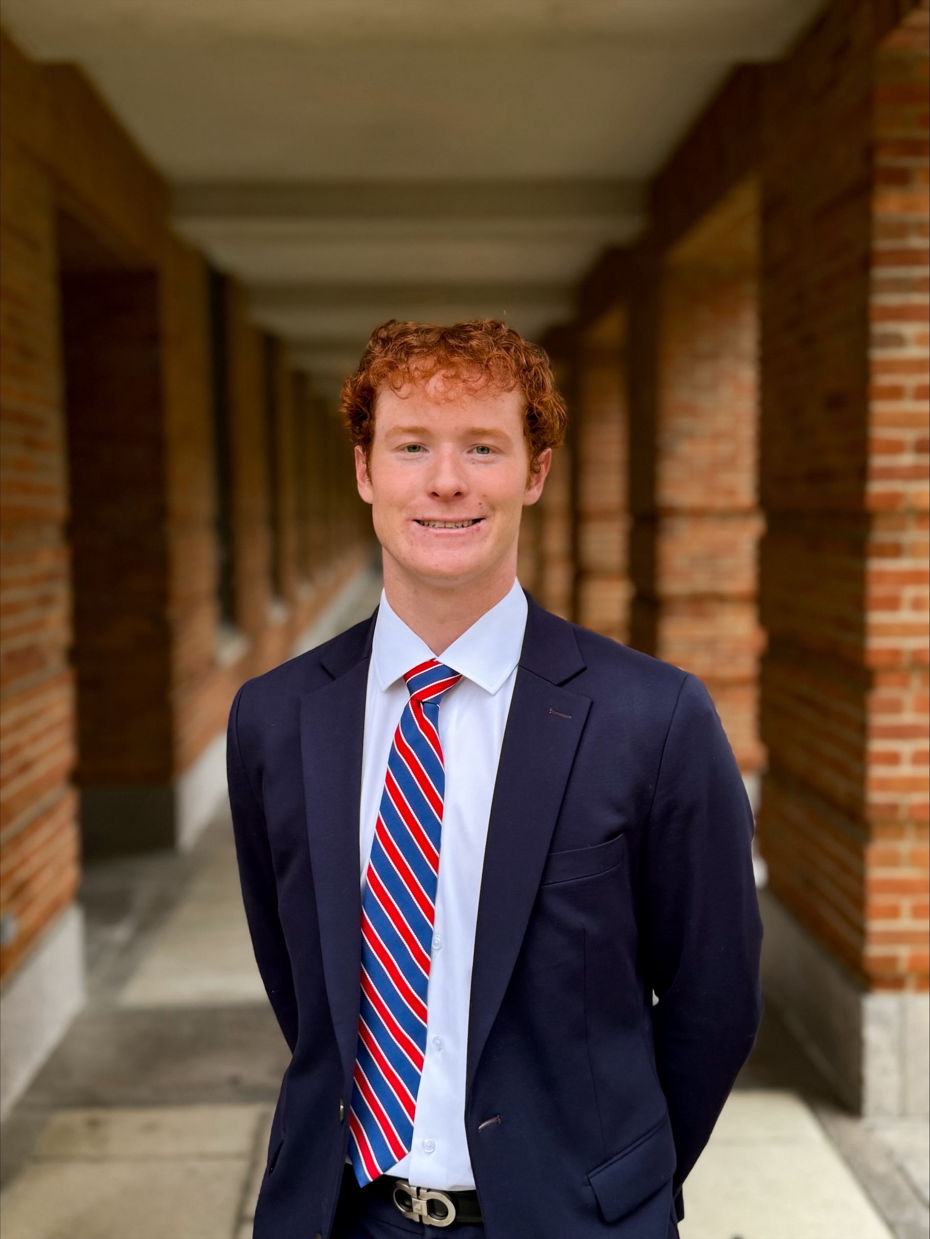 man smiling at camera with navy blue tux and blue and red tie