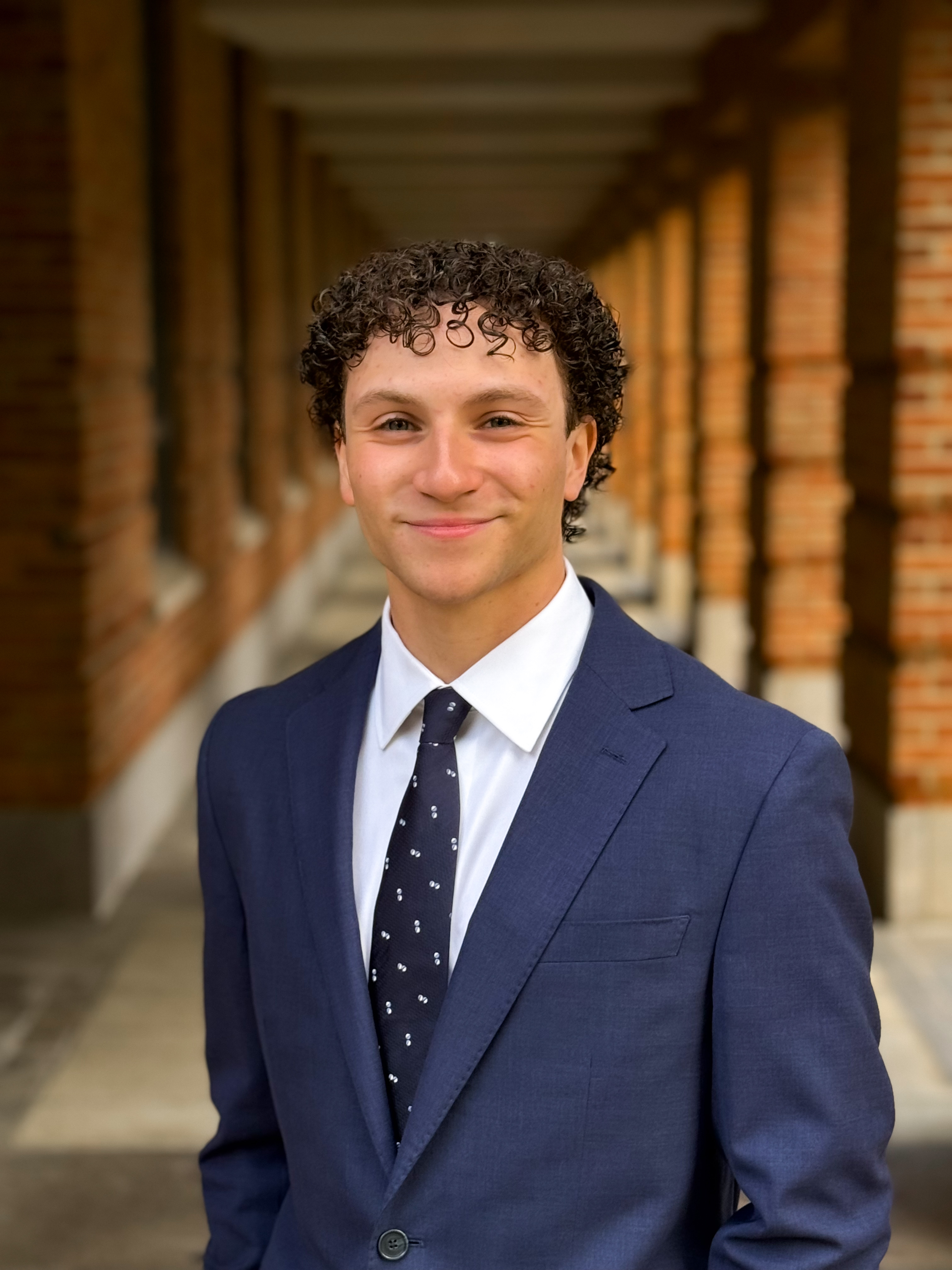 man with curly hair smiling at camera with navy blue suit